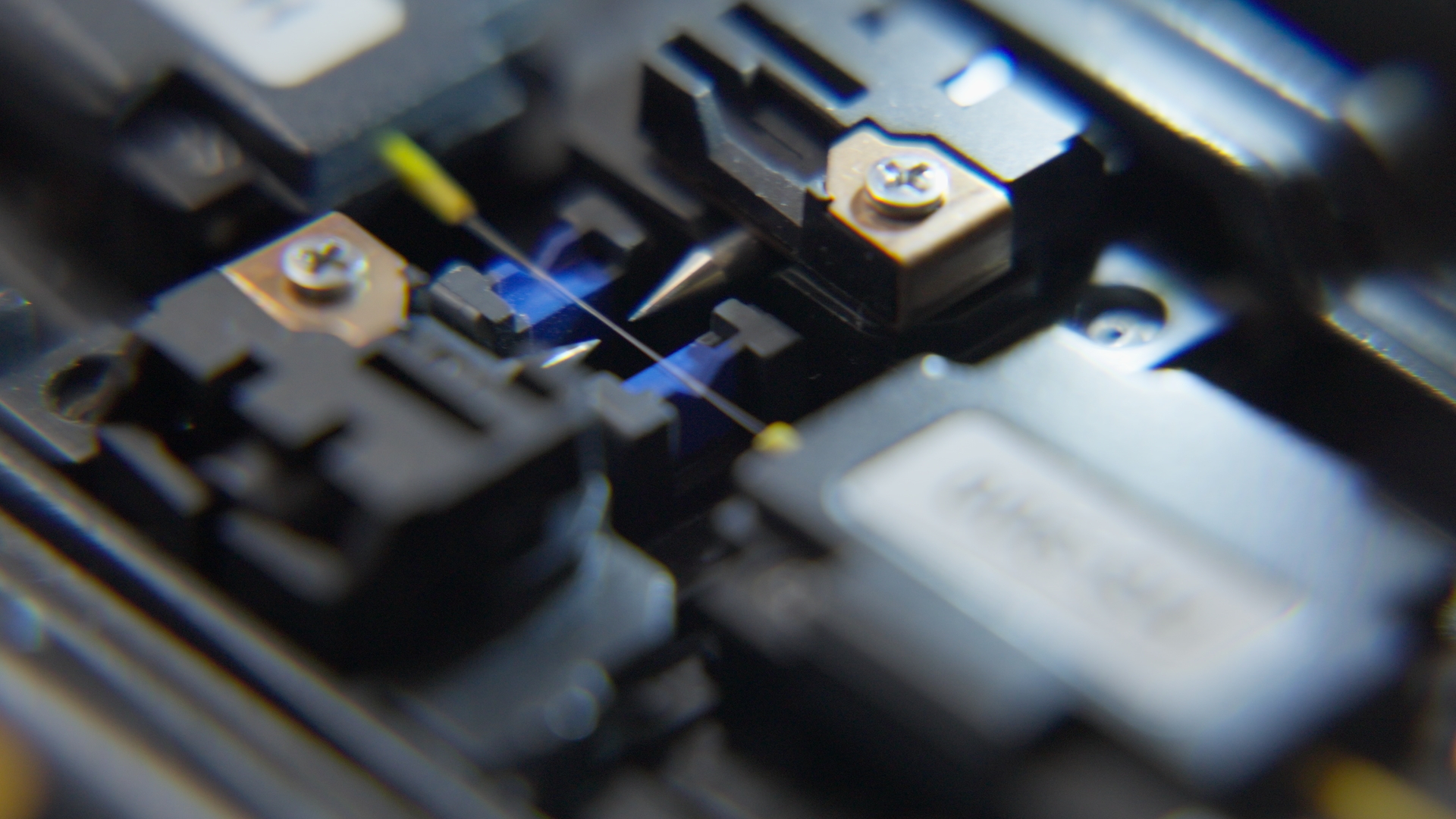 Macro photograph of a fiber optic fusion splicer aligning two bare optical fibers between electrodes during manufacturing.