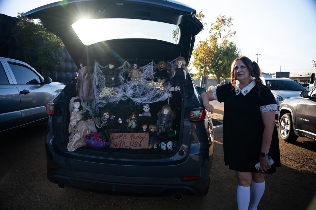 Attendee in a black dress and white socks beside a decorated SUV trunk at Trunk or Treat