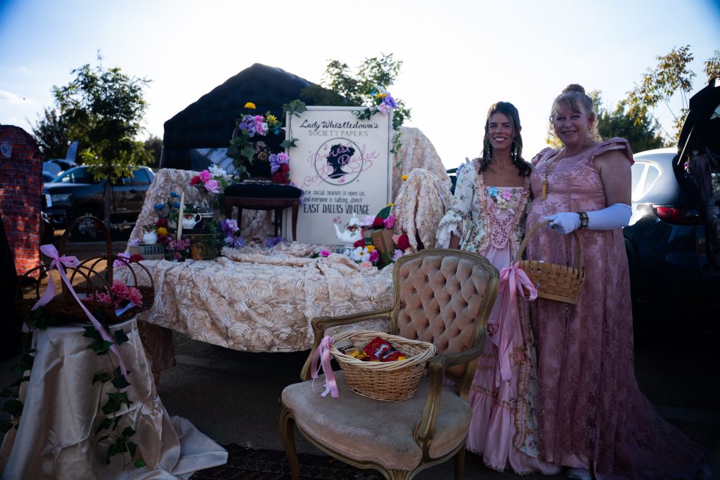 Two women in pink period gowns beside an elegant tea party display at Trunk or Treat