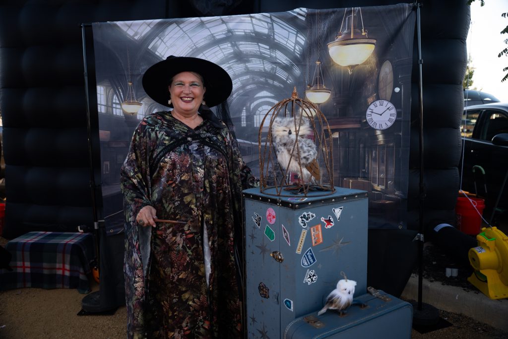 Woman dressed as a witch beside a spooky themed display at the Lake Ridge Village Trunk or Treat