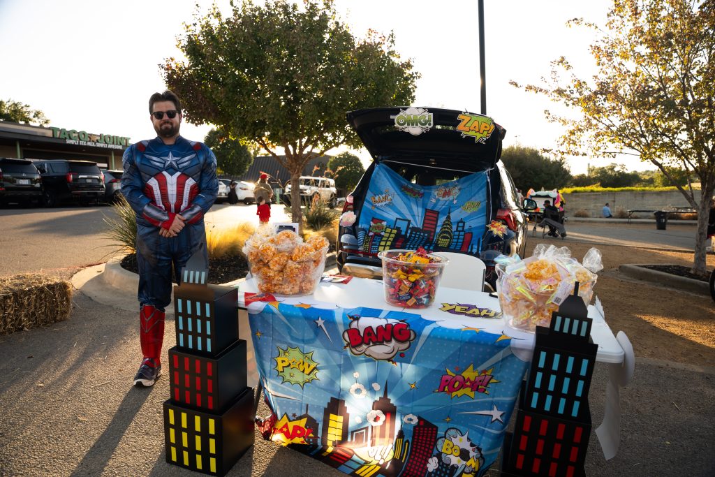 Man dressed as Captain America beside a comic book-themed trunk display at Trunk or Treat