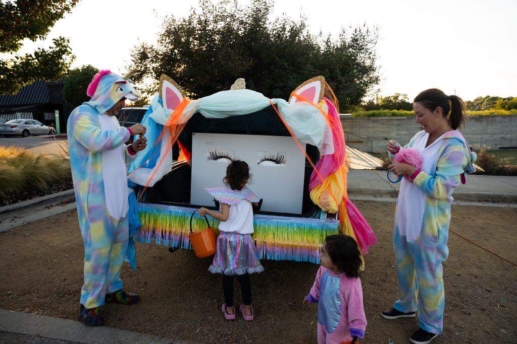 Child collecting candy at a unicorn-themed trunk with hosts in unicorn costumes at Trunk or Treat