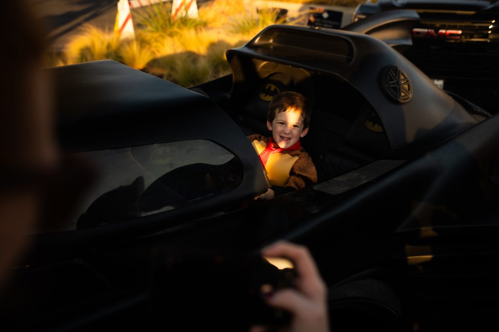 Child in costume smiling from inside the Batmobile at Trunk or Treat, Lake Ridge Village