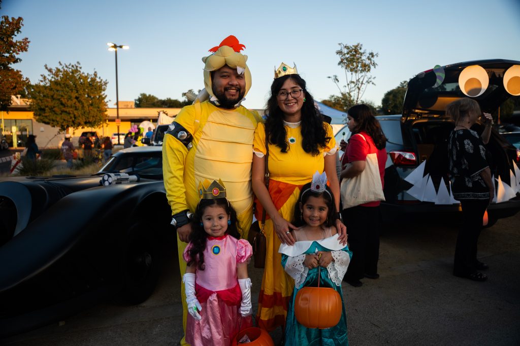 Family in Super Mario-themed costumes posing near the Batmobile at Trunk or Treat